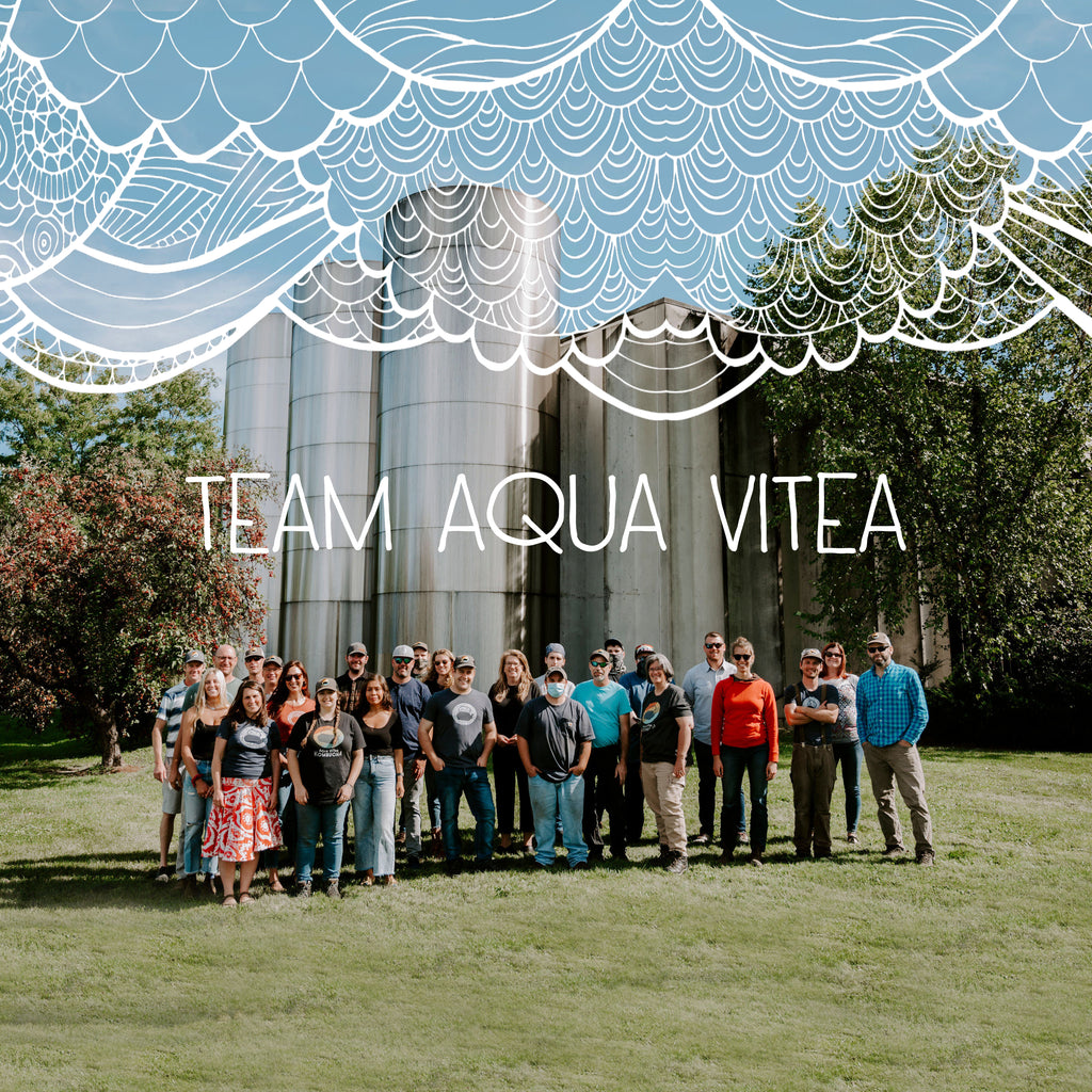 The Aqua Vitea staff outside their production facility with 'TEAM AQUA VITEA' written across the image and lacy/scaled drawn in decoration at the top