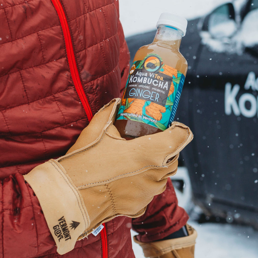 Hand holding a bottle of ginger kombucha in the snow