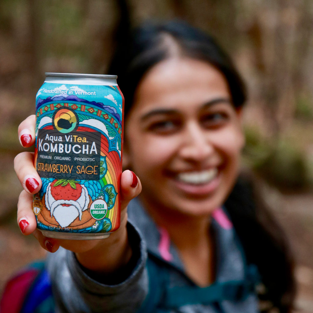 person smiling holding a strawberry sage kombucha can up close to the viewer